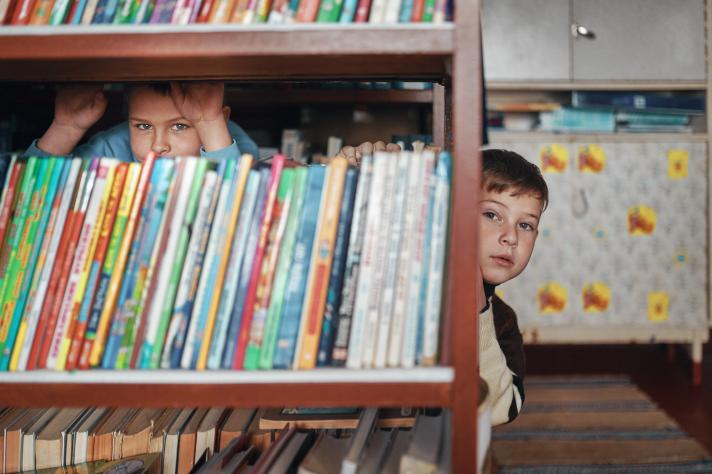 A book rack with behind it 2 children peeping out.