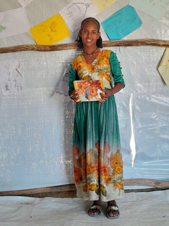 Wegahta, standing in front of a classroom wall with papers and drawings on it.