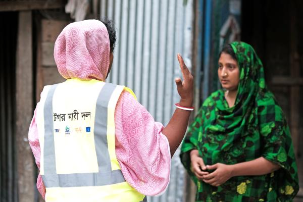 Sajia Akhter standing in her doorway, an aid worker is talking with her.