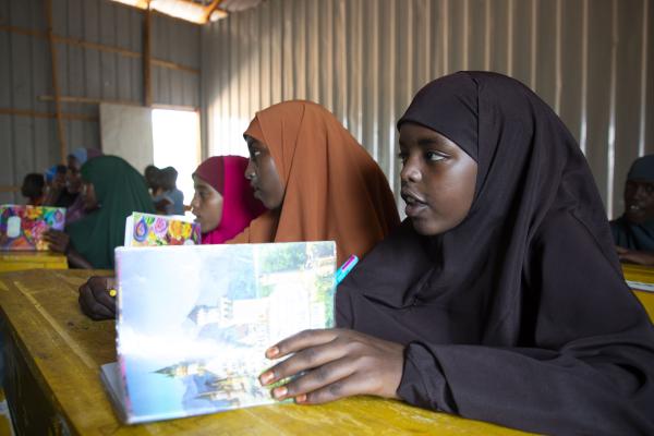 3 students at a desk, holding a book.