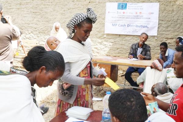 People receiving cash assistance. Some standing at a table, others seated at the table.